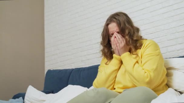 Woman in sweater sits on bed and coughs and sneezes. She has cold, flu, coronavirus. Her throat hurts. She has fever and she wraps herself in blanket. Flu, cold, coronavirus epidemic isolation — Stock Video