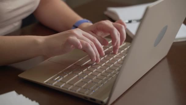 Ženské ruce píší text na klávesnici notebooku. Prsty rychle stiskněte klávesy na klávesnici. Vedle něj je zápisník. Osobní počítač, vzdálená práce doma, obchod, studie, zprávy, chat — Stock video