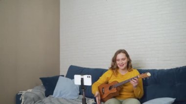 Kadın çevrimiçi bir ders veriyor ve öğrencilere ukulele çalmayı öğretiyor. Gitarı elinde tutuyor ve insanlara canlı video bağlantısıyla anlatıyor. Bloglama, tecrit, çevrimiçi eğitim