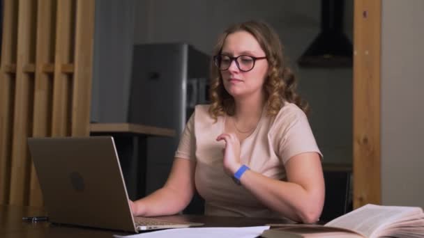 Woman with glasses is sitting at desk and working at home, she bends down and holds her head, she is tired and yawns. Overtime, laziness, insomnia, boredom, e-learning, distance, quarantine, pandemic — Stock Video