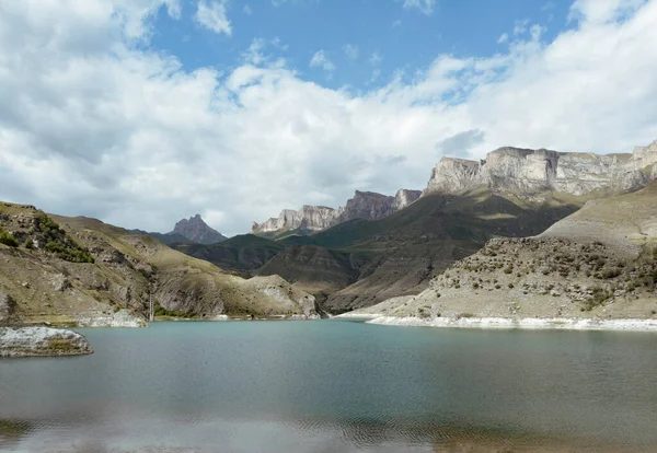 Luftfoto af azurblå bjergsø Gizhgit, Kaukasus. Blå vand skinner i sollys. Høj majestætisk bjergkæde er synlig. Skarpe toppe af toppe gløder mod den overskyede himmel. Drone videooptagelse Stock-foto