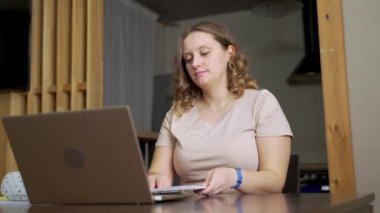 Kadın masada oturuyor, gözlüklerini takıyor ve çalışmaya başlıyor. Çalışma gününün başlangıcı. E-öğrenme, internet üzerinden uzaktan çalışma, evde çalışma, mesafe, salgın