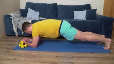 Şişman adam kilo vermek için fiziksel egzersiz yapıyor. Dirsekleri üzerinde kalas pozisyonunda duruyor ve gerilimden titriyor. Evde eğitim, karantina, salgın hastalık. Kilo kaybı, sağlıklı yaşam tarzı.