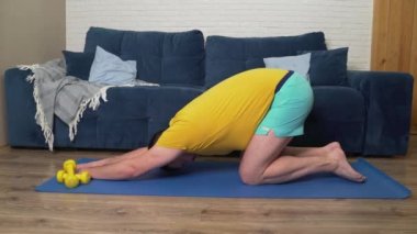 Sakallı tombul adam kilo vermek için fiziksel egzersiz yapıyor. Paspasın üzerine oturur ve elleriyle ileri doğru uzanır. Evde eğitim, karantina, salgın hastalık. Kilo kaybı, sağlıklı yaşam tarzı.