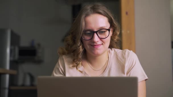 Femme avec des lunettes est assis à l'ordinateur portable et textos avec quelqu'un ou la préparation de rapport de travail. Elle va bien et de bonne humeur. E-learning, travail à domicile, quarantaine, distance — Video