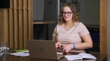 Gözlüklü kadın masasında oturuyor ve evde çalışıyor, iş arkadaşları ve arkadaşlarıyla bilgisayarda video üzerinden iletişim kuruyor. E-öğrenme, video iletişimi, karantina, uzaktan öğrenme