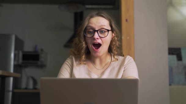 Mujer con gafas ha ganado la lotería o pasó un examen y es feliz. Mira el monitor y de repente comienza a regocijarse. Agita los brazos, aplaude, baila. Ganar la lotería, pasar el examen, obtener buenas noticias — Vídeos de Stock