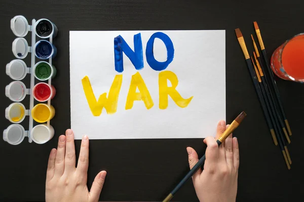 Man paints poster for rally with the slogan NO TO WAR. With brush and paints, he prints colorful bright letters on sheet. Persons requirement. Poster with call, rally, picket, march, protest, action