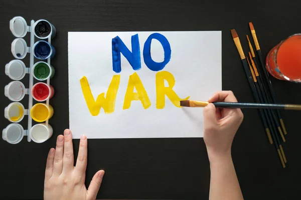 Man paints poster for rally with the slogan NO TO WAR. With brush and paints, he prints colorful bright letters on sheet. Persons requirement. Poster with call, rally, picket, march, protest, action