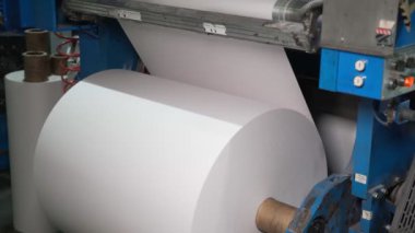 Paper for printing newspapers and magazines. A large bobbin with a roll of white paper is spinning on the machine. Printing house, publishing house. Media, article, headline, daily news, print edition