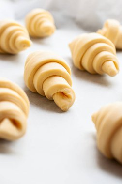 Semifinished or unbaked croissant on a baking sheet. Puff pastry baking. Close up.