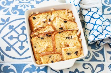 Bread (panettone) pudding from leftovers with custard and raisins in a baking dish on a blue background. Top view.