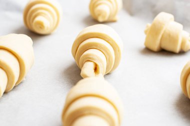 Semifinished or unbaked croissant on a baking sheet. Puff pastry baking. Close up.