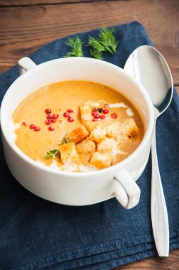 Kremalı balkabağı çorbası ve ahşap masada beyaz bir kasede kızarmış ekmek. Kapat.