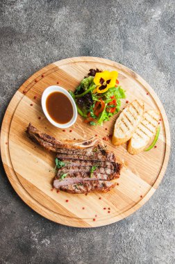 Gri arka planda ahşap bir tahtada ızgara biftek. Üst görünüm.