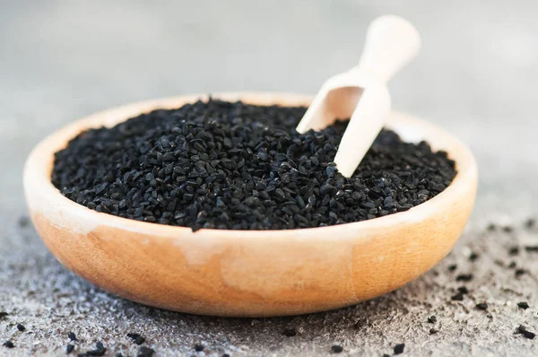 Siyah kimyon ya da nigella sativa tohumları gri arka planda tahta bir tabakta. Kapat..