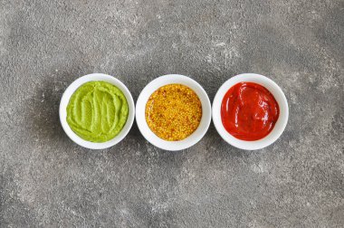 Üç çeşit sos, Fransız hardalı, ketçap ve gri arka planda guacamole..