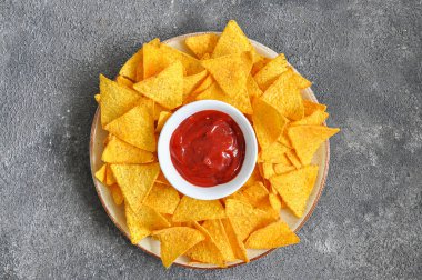 Büyük tabakta mısır cipsi ve gri arka planda ketçap sosu. Üst ivew.