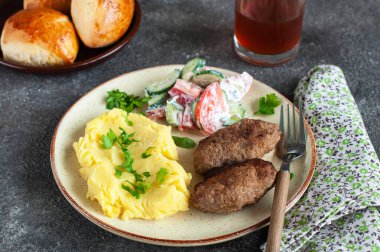 Ev yapımı et pirzolası, patates püresi ve sebze salatası, gri bir arka planda..