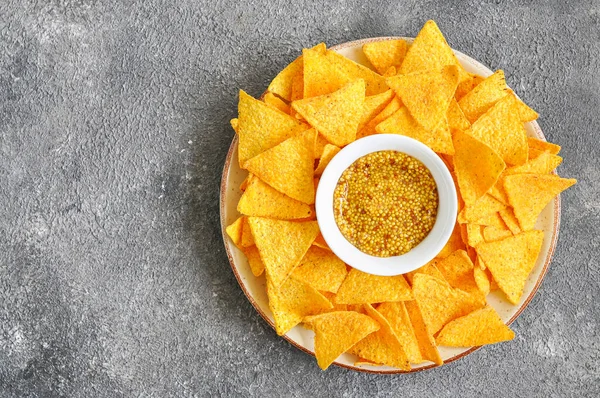 Corn tortilla chips with french mustard served in big plate on a gray background. Top ivew.