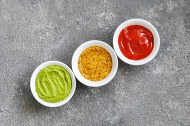 Çeşitli soslar, Fransız hardalı, ketçap ve gri arka planda guacamole. Üst görünüm.