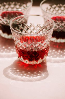 Pembe arka planda soyut gölgeler olan şeffaf bardakta kırmızı şarap.. 