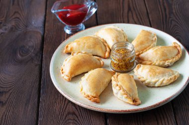 Tabakta taze pişmiş küçük börekler ketçap ve ahşap bir arka planda hardal..