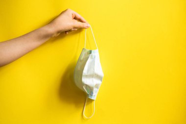 Bir kızın elinde tıbbi maske. Sarı arkaplan.