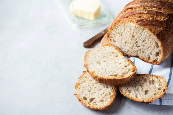 stock image Homemade artisanal sliced sourdough bread on a napkin and butter with knife. Healthy home baking concept.