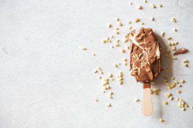 Çatlak vanilyalı bademli dondurma ve gri bir arka planda çikolata jöleli tahta çubuk. Üst görünüm.