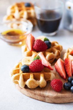 Waffles with berries and honey and coffee on a wooden board. Close up and copy space. 