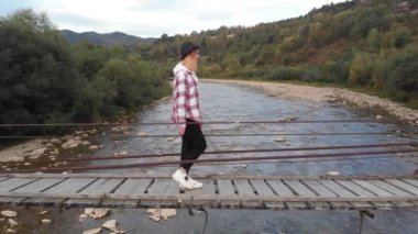 Turist kadının dağ nehri boyunca tahta köprüde yürüdüğü hava manzarası. 