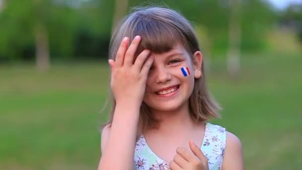Entzückendes kleines Mädchen lächelt in die Kamera mit Wangen, die in Frankreich-Flagge gemalt sind. Bastille-Tag am 14. Juli. Der Tag Frankreichs. — Stockvideo