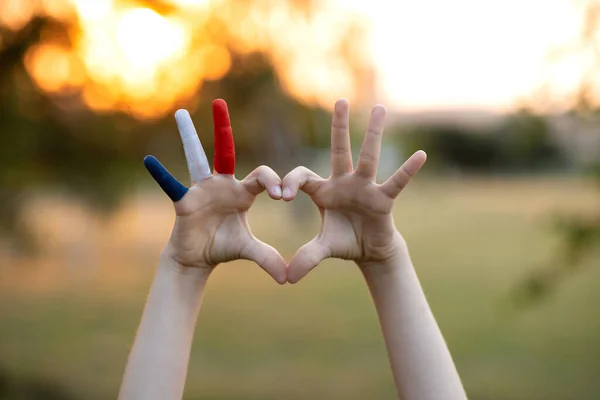 Manos de niño pintadas en color de la bandera de Francia formando un símbolo del corazón y el amor gesto al aire libre —  Fotos de Stock