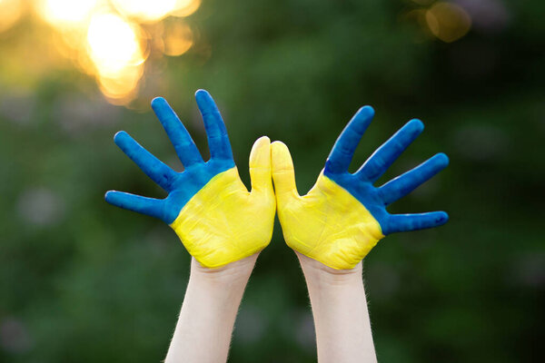 Маленькая школьница показывает руки, окрашенные в желтый и синий цвета. Детские руки, выкрашенные в синий и желтый флаг Украины. День флага Украины. День Конституции. 24 августа. Патриотический праздник