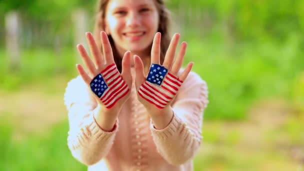 かわいいティーンエイジャーの女の子は、アメリカの国旗の色で描かれた手で挨拶を振って。アメリカは７月４日を祝う。独立記念日 — ストック動画