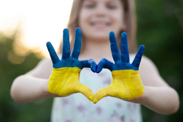 Forme de coeur avec des mains d'enfant du langage corporel de l'enfant, gentillesse, concept d'amour patriote. Coeur main sur coucher de soleil ciel bokeh fond peint en couleurs drapeau ukrainien — Photo