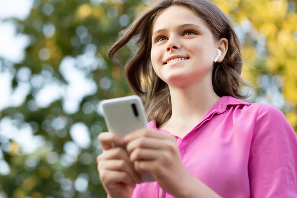 Chica bonita llena de alegría lleva en rosa consiguen llevar con la música. Asiática adolescente chica uso de teléfono inteligente y disfrutar de lista de reproducción favorita a través de auriculares estéreo, canta relajado junto con la expresión despreocupada. — Foto de Stock