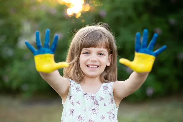 Радостная девушка, размахивая руками, раскрашенными в цвета флага Украины и здороваясь на закате — стоковое фото