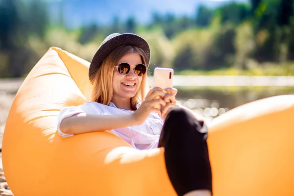 Retrato de la encantadora mujer sonriente en gafas de sol utilizando el teléfono celular y escribir mensajes a amigos mientras está acostado en el colchón de aire en la playa de verano — Foto de Stock