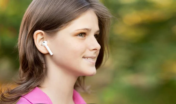 Retrato de chica encantadora en rosa escuchando música a través de auriculares inalámbricos al aire libre. Jovencita sonriendo feliz. Aerópodos. Imagen De Stock