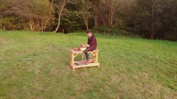 Instantánea orbital aérea de cerámica artista de cerámica concentrado en el trabajo con la rueda de arcilla al aire libre en el prado verde en la puesta del sol increíble. Taller creativo que conforma o esculpe. Habilidades motoras finas — Vídeo de stock