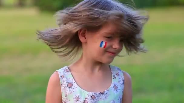 Gyermek vidám lány boldogan rázza fejét az arcát festett a zászló Franciaország, a haja repül a különböző irányokba. Lassú mozgás vicces nevető kis szőke gyerek lány 6-8 éves szabadban — Stock videók