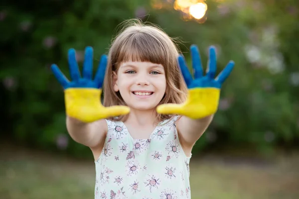 Chica alegre agitando las manos pintadas en colores de la bandera de Ucrania y decir hola al aire libre al atardecer —  Fotos de Stock