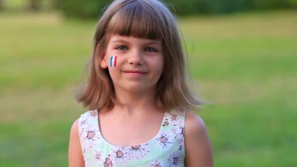 Adorable petite fille sourire à la caméra avec les joues peintes en drapeau de France. Jour de la Bastille le 14 juillet. Le jour de la France. — Video