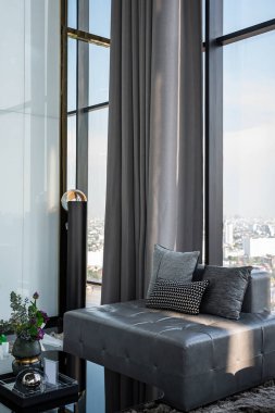 29. kattaki lüks dairenin oturma odasında büyük kare bir kanepe ve üç yastık. Şehre bakan çıplak bir cam duvar var..