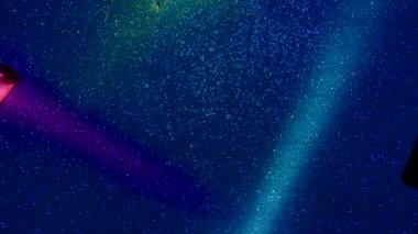 Multi-colored beams of light blink on a dark background.