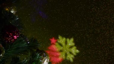 Noel ağacı şenlikli toplarla süslenmiş. Renk değiştiren yanıp sönen bir arkaplanda farklı renklerde ışık huzmeleri. Noel ağaçlarının ve kar tanelerinin uçan renkli siluetleri.