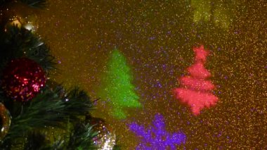 Noel ağacı şenlikli toplarla süslenmiş. Renk değiştiren yanıp sönen bir arkaplanda farklı renklerde ışık huzmeleri. Noel ağaçlarının ve kar tanelerinin uçan renkli siluetleri.