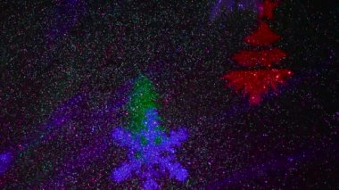 A carousel of light beams of different colors is set against a constantly flashing background that changes colors. Flying colored silhouettes of Christmas trees and snowflakes.